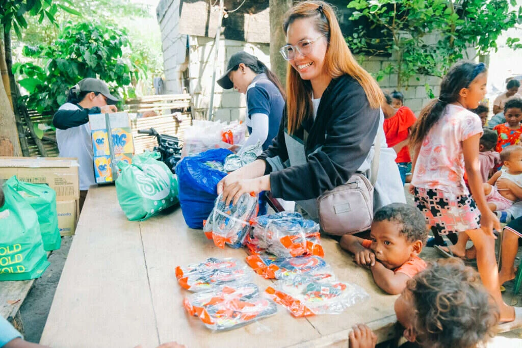A volunteer sorting packages on a wooden table while children watch