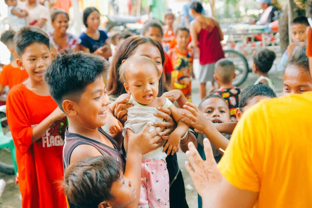 A boy laughing while holding a baby up in a crowd of children